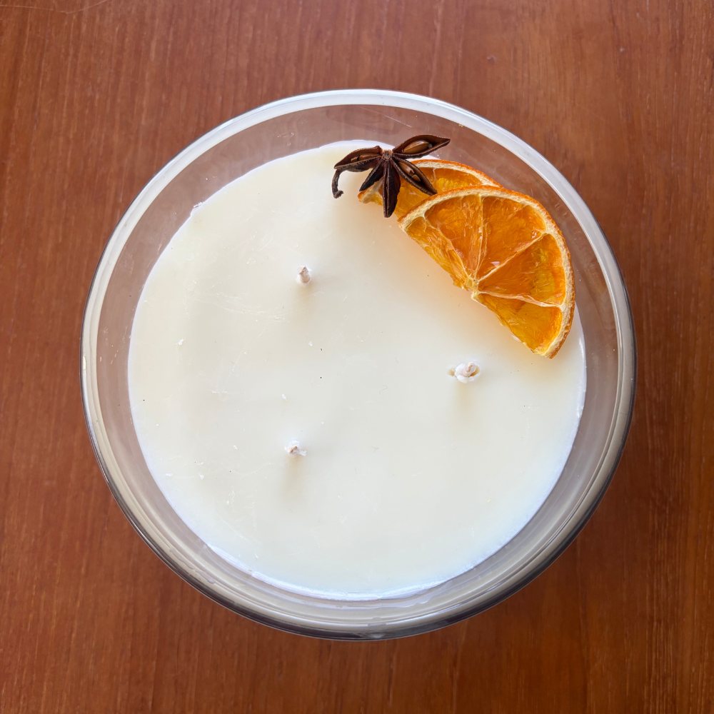Candle in a glass jar with an orange slice and star anise on a wooden surface